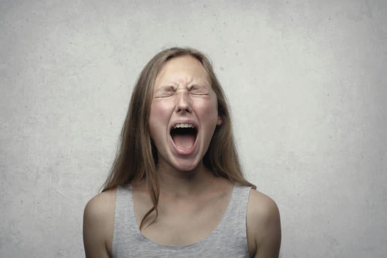 Une femme, en débardeur gris, crie avec une expression de colère