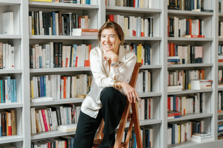 Valérie Gans, assise sur une échelle devant une grande bibliothèque