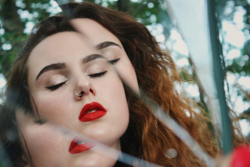 Une femme ferme les yeux devant un miroir cassé