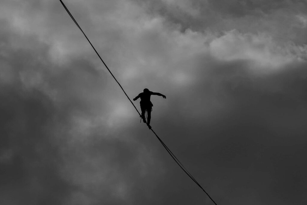 Un homme fait l'équilibriste sur une corde dans le vide, la photo est en noir et blanc