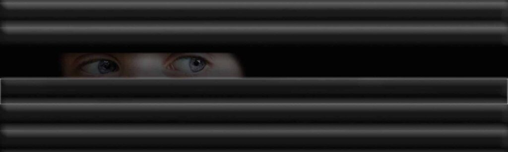 Une personne se cache derrière un store d'une fenêtre