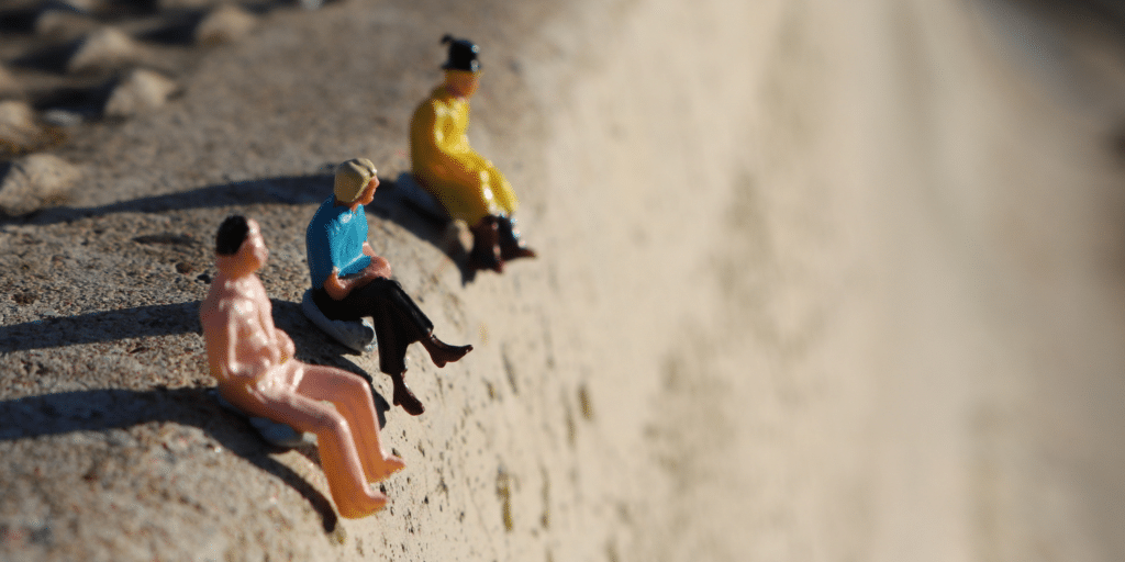 UneAutreVoix-EcritureInclusive-GensGouffre | Une Autre Voix Des figurines assises contemplatives sur un trotoire en béton qui paraît être un mur très haut