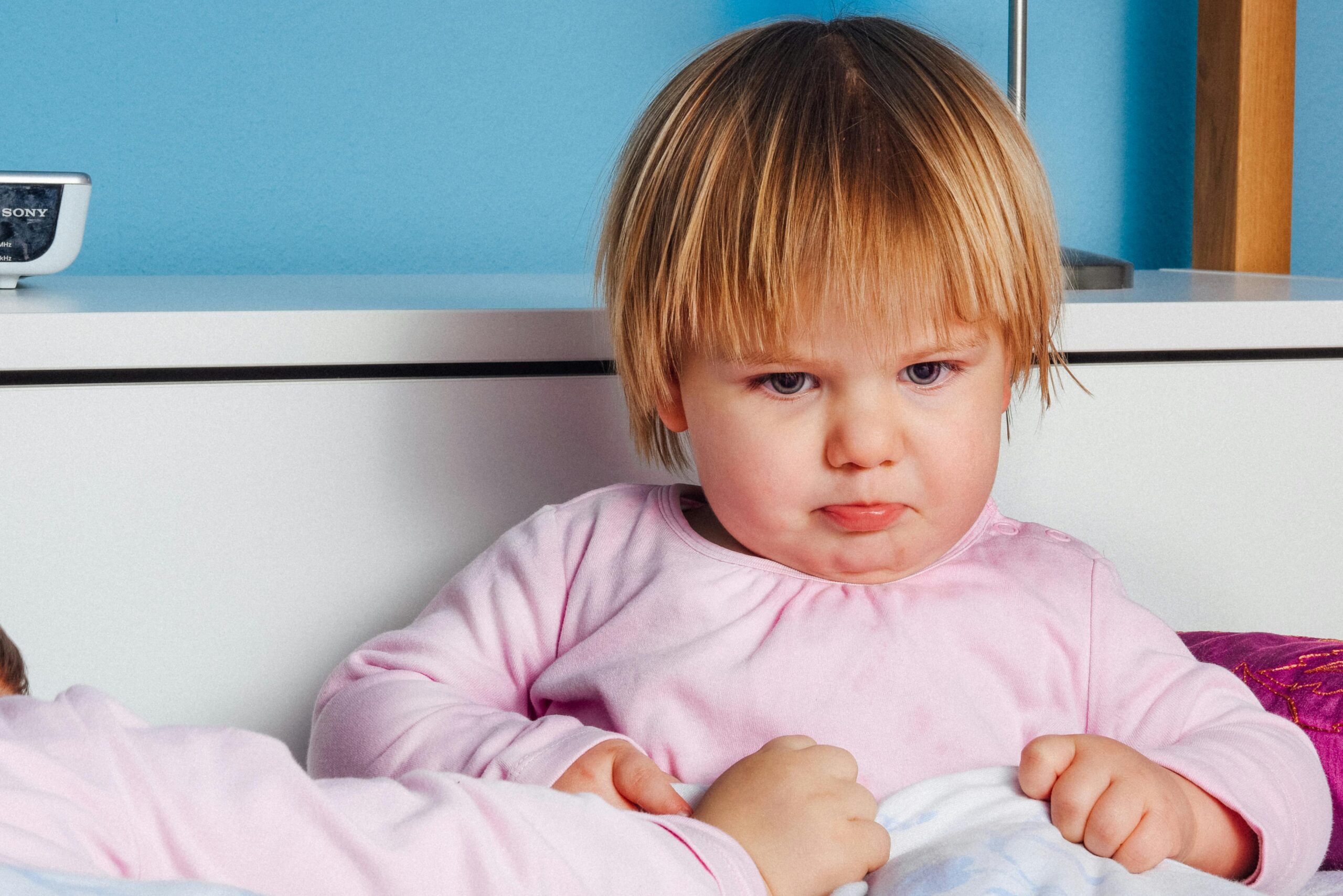 Un enfant aux cheveux blonds et raid en chemise rose regarde devant lui avec une expression d'énervement à la limite des pleurs