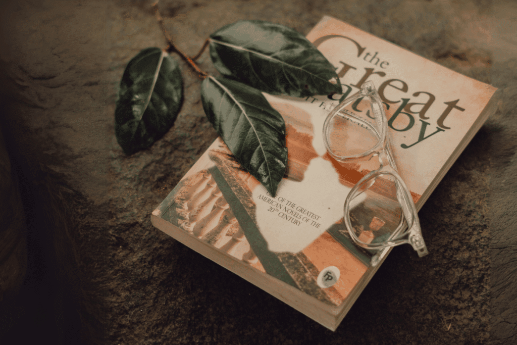 Le livre "The Great Gatsby" sur le sol avec des lunettes et des feuilles posées dessus