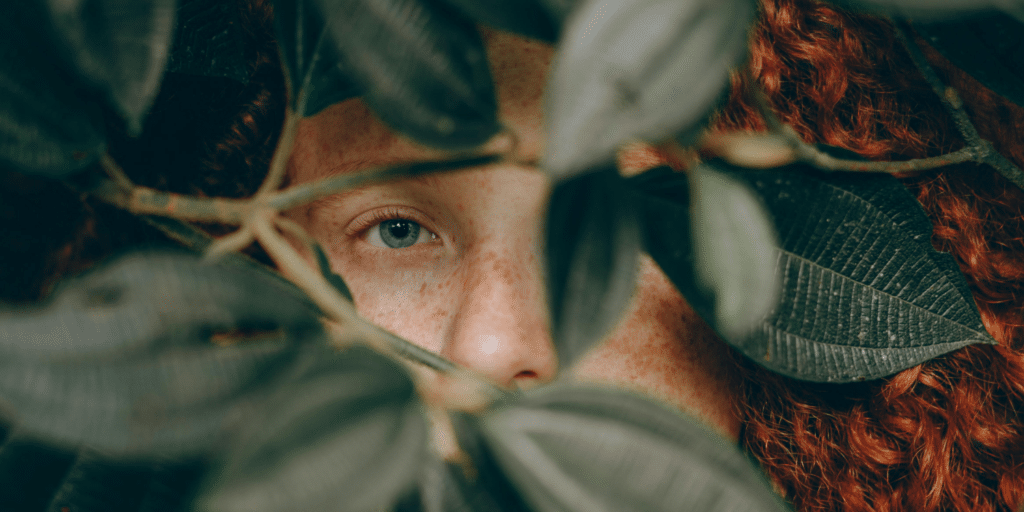 Une femme se cache derrière un buisson, on ne voit que son regard et un bout de son nez