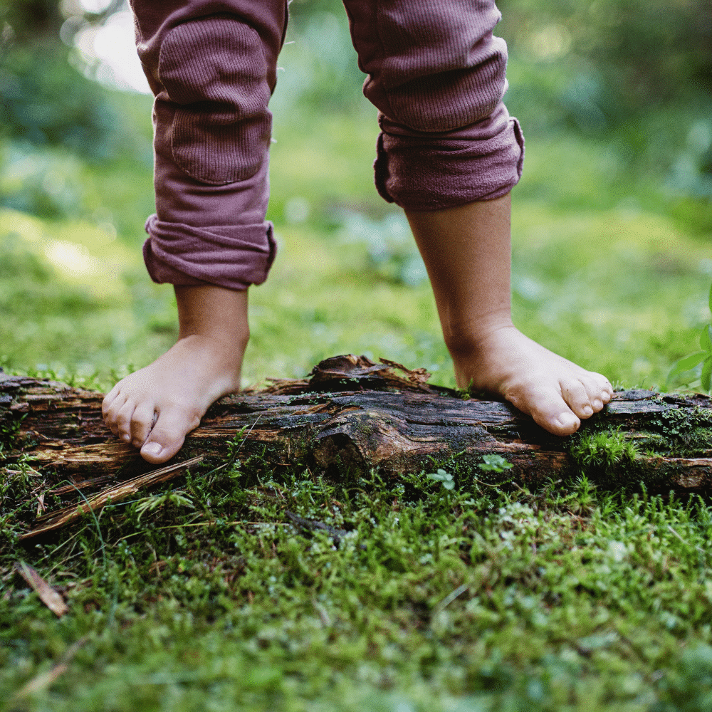 Un enfant est debout sur un bout de bois au sol, les pieds nus