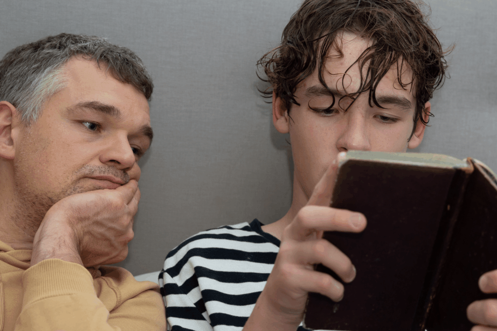 Un jeune homme lit un livre et un autre homme plus âgé lit par-dessus son épaule