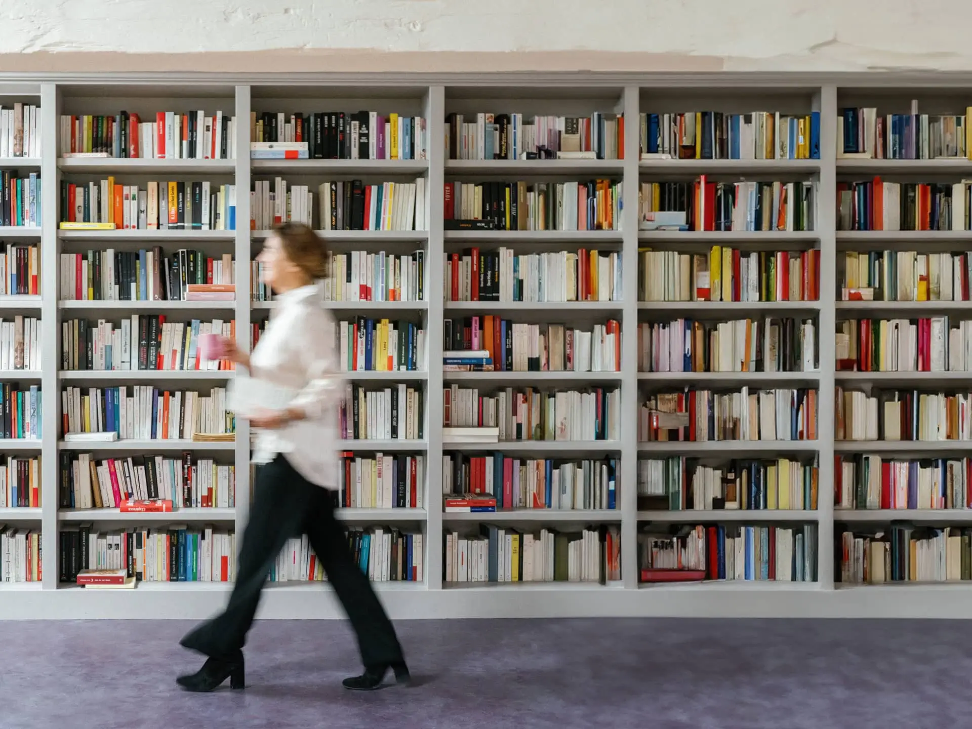 Valérie Gans marche devant une bibliothèque