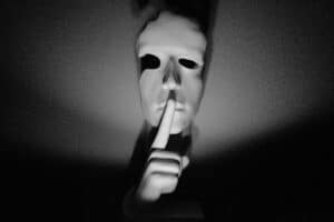 Une personne masquée fait "chut" avec sa main