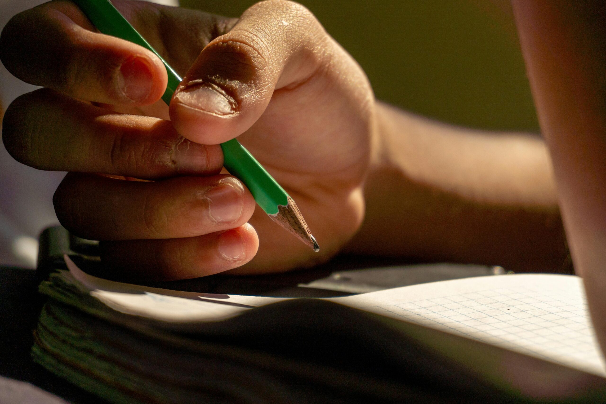 Une personne tient un crayon dans sa main au-dessus d'un cahier
